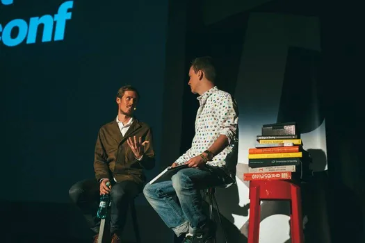 Edvard Scott (left) in an on-stage conversation, beside a stack of design books on a red stool