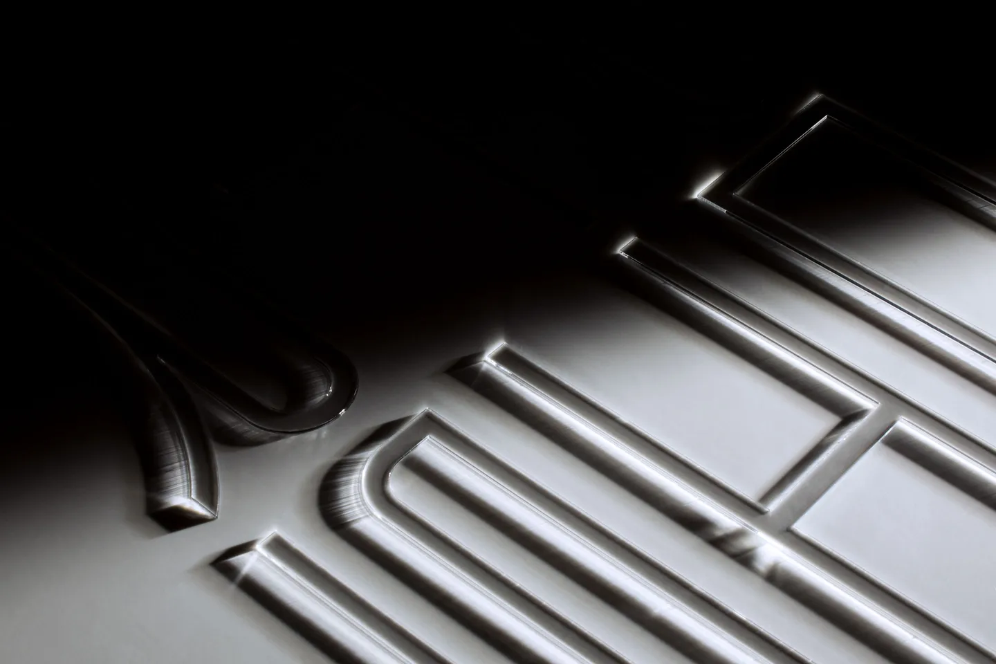 Close-up of letterforms laser-cut into a white surface, lit at a raking angle from the dark