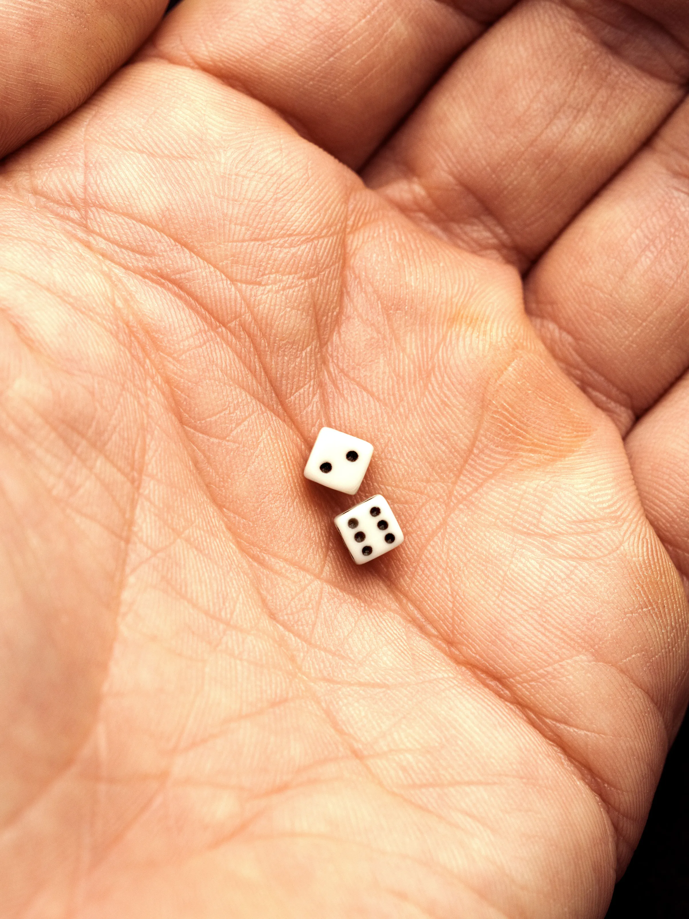 Open palm, close up, holding two tiny white dice showing two and six