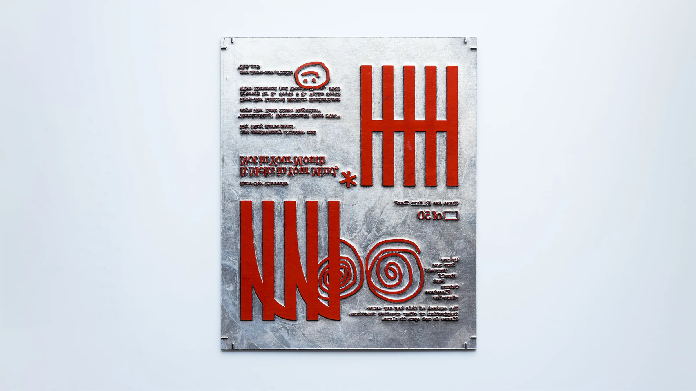 Printing plate with raised red Here-Now glyphs, spirals and mirrored “It Melts In Your Mind, Not In Your Mouth”