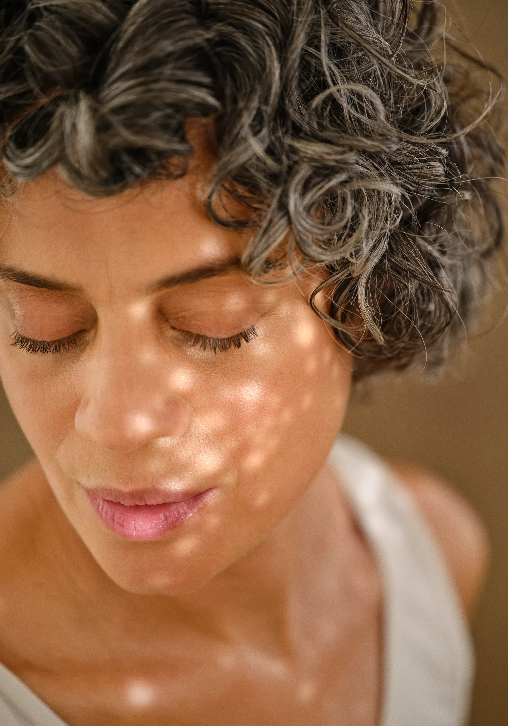 Olink campaign portrait: a woman with curly grey hair, eyes closed, in dappled light