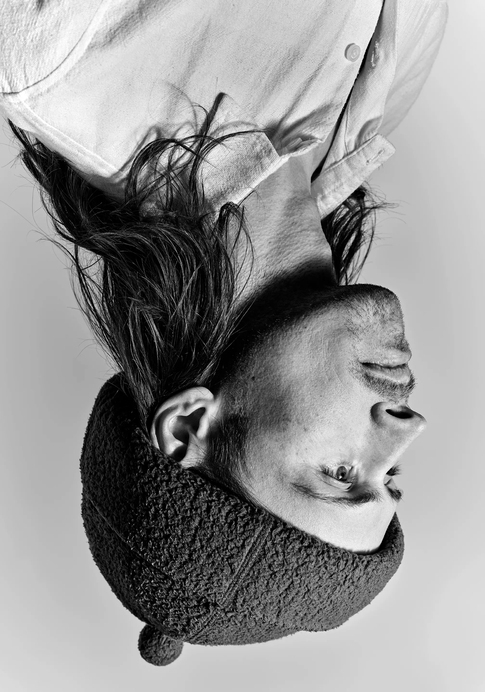 Black-and-white portrait, shown upside down, of a long-haired person in a fleece hat