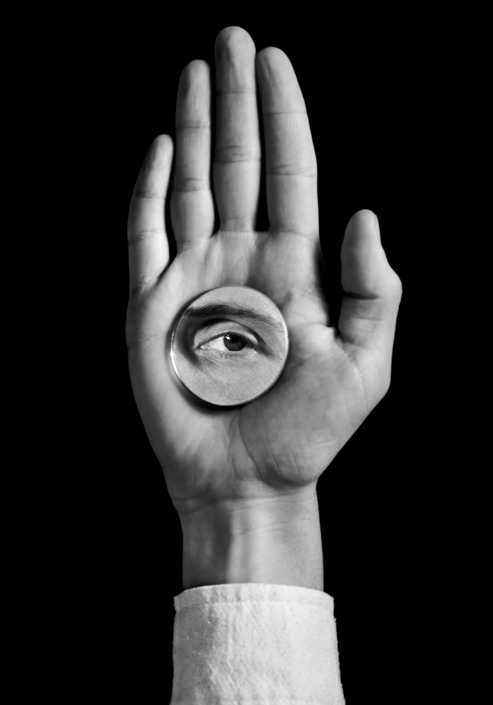 Black-and-white photo of an open palm holding a round lens that magnifies an eye