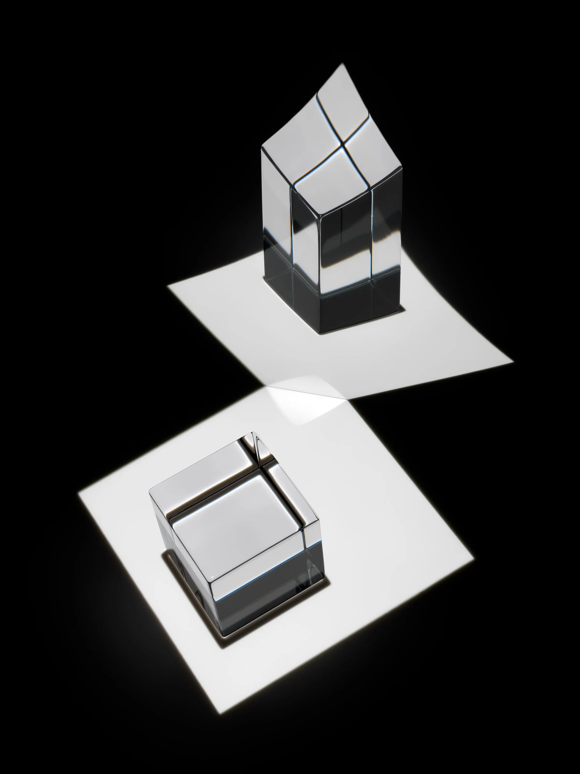 Two glass cubes, each standing on a white sheet of paper, lit hard against black