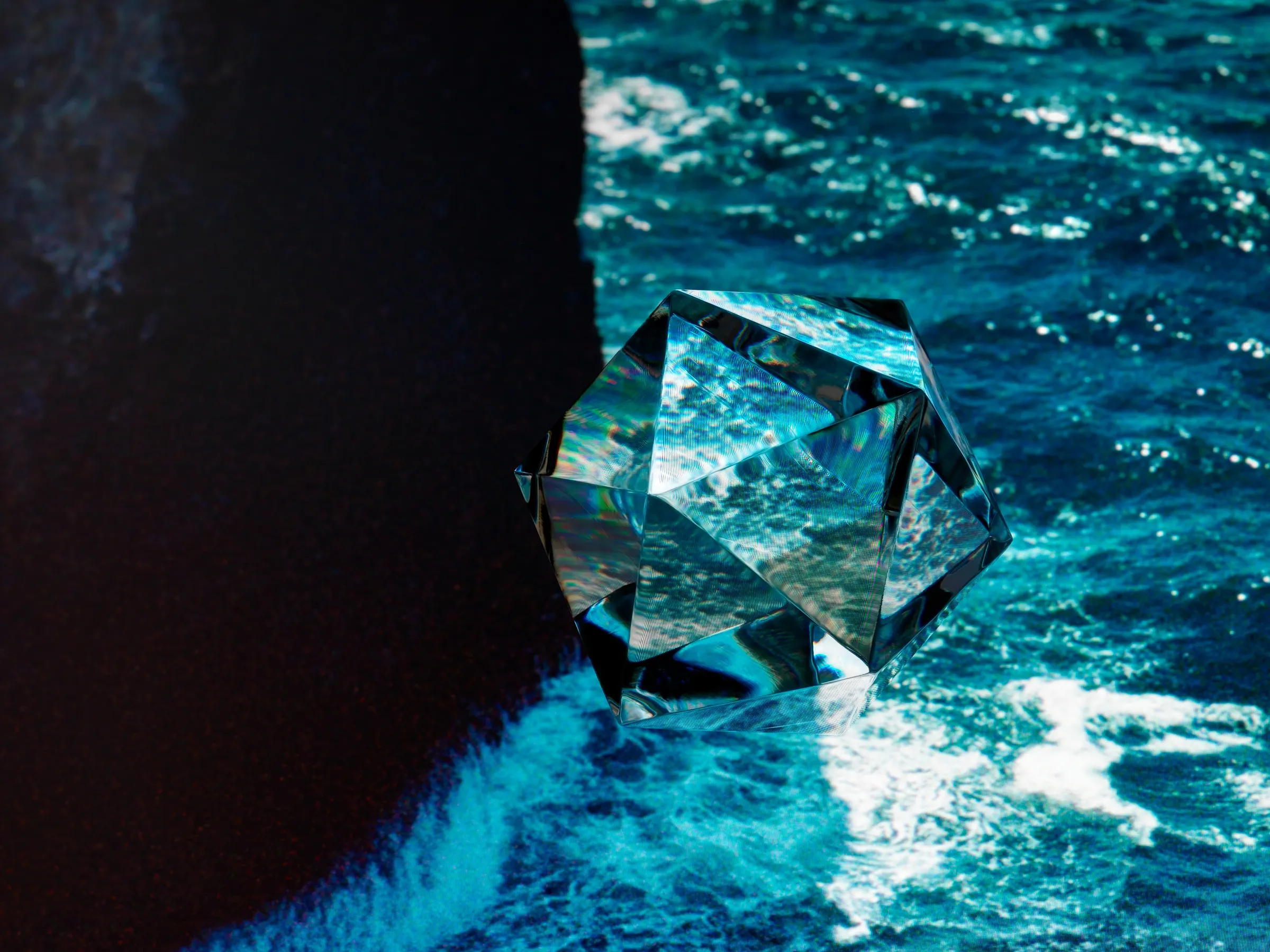 A glass icosahedron on a black rock at the edge of a blue, breaking sea
