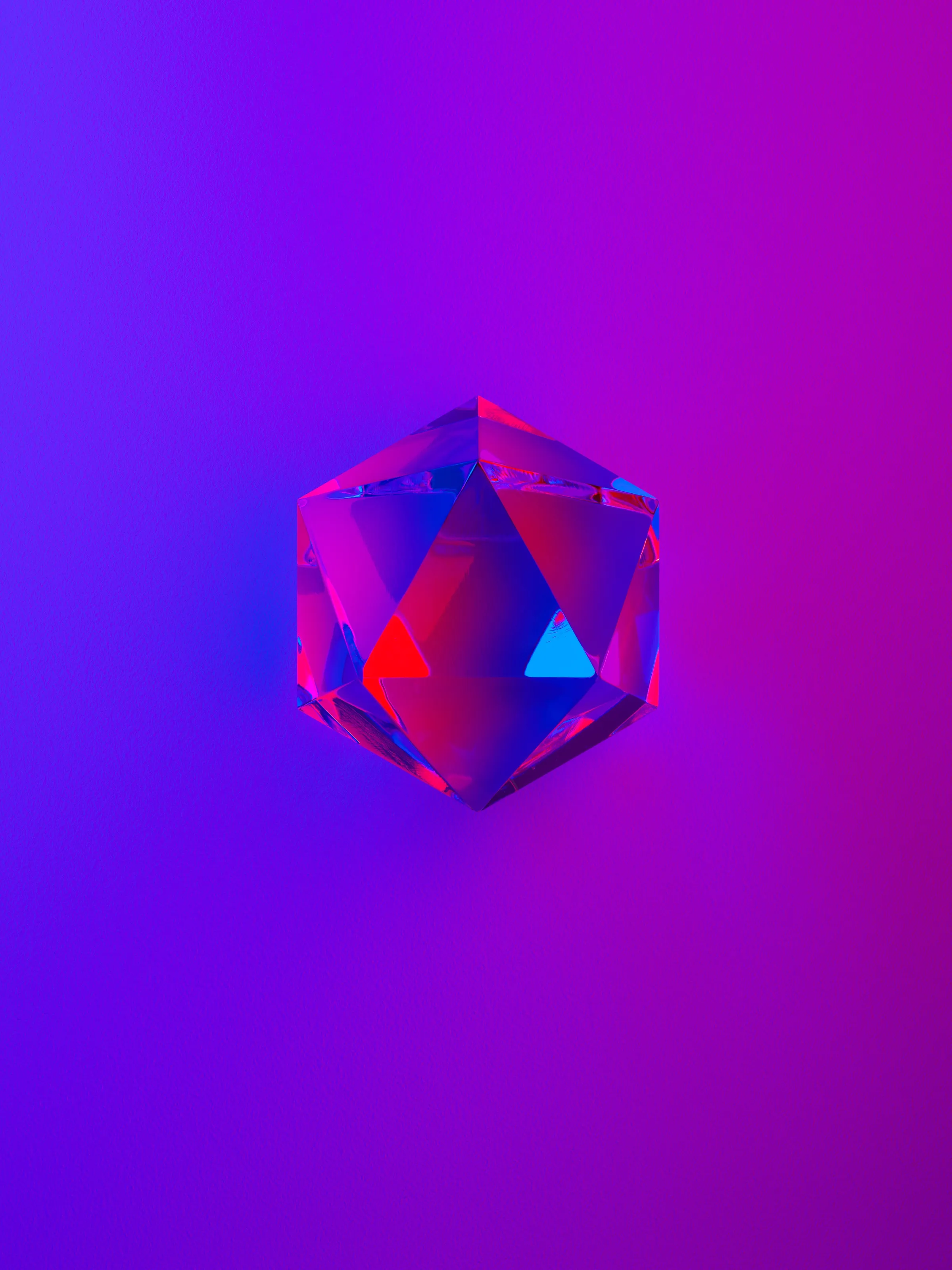 A glass icosahedron catching red and blue light on a violet-to-magenta gradient