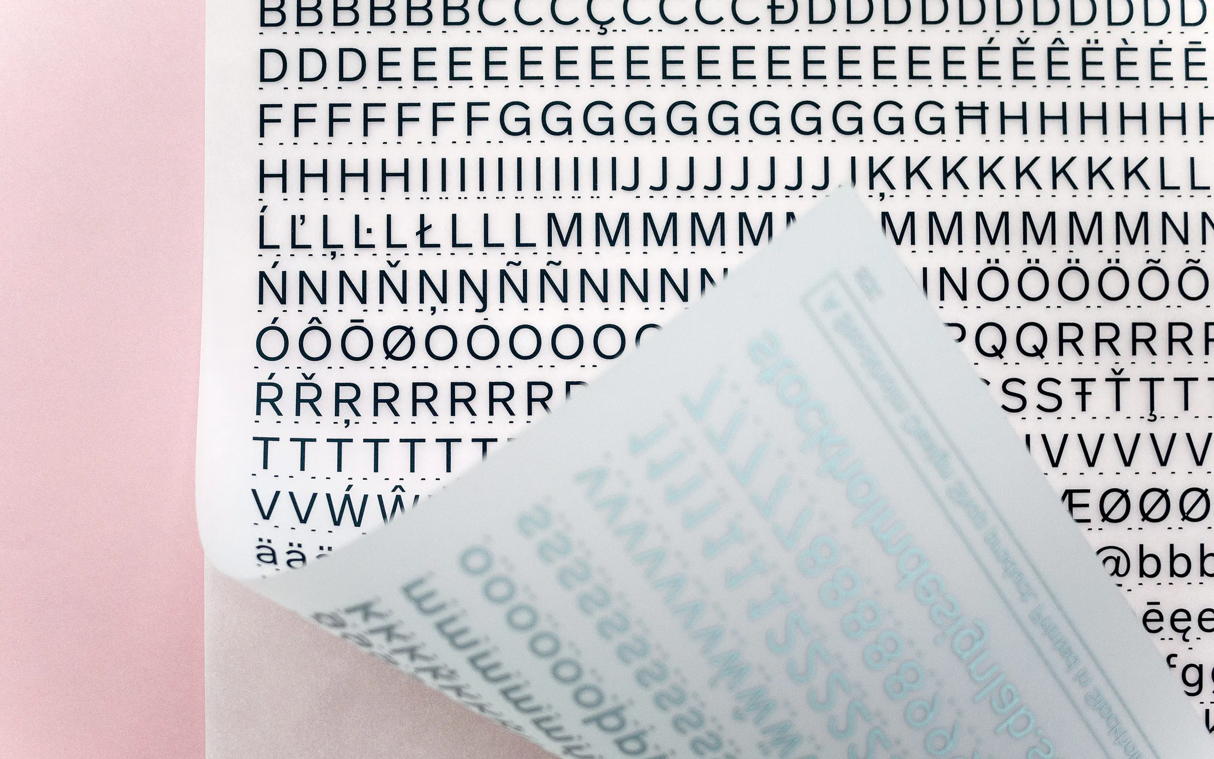 Sheet of black rub-down capitals and accented letters, its translucent backing peeled back at one corner