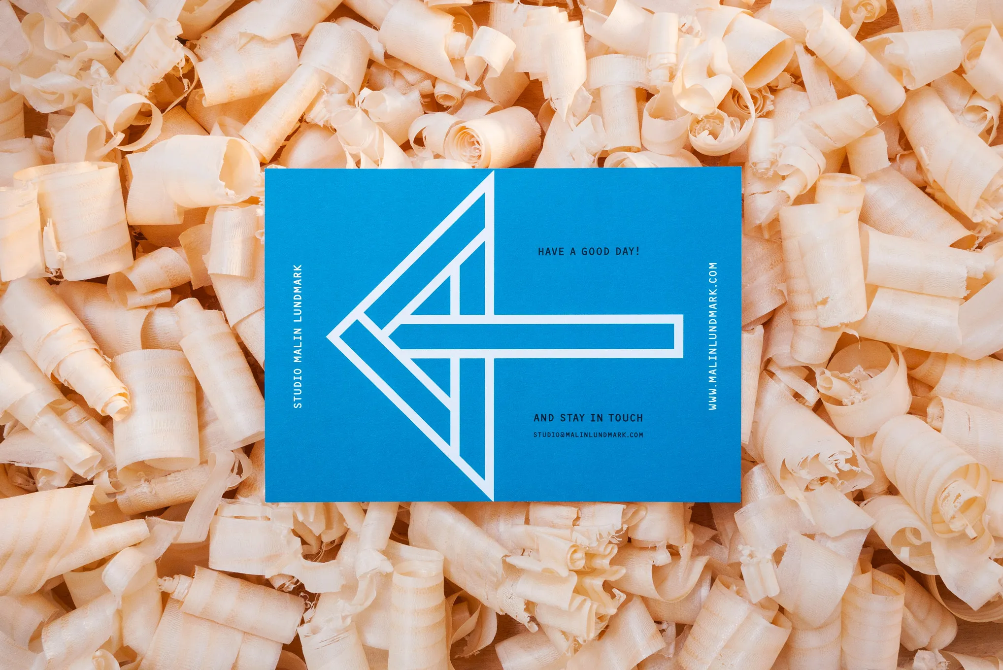 Blue card with a white outlined arrow and “Have a good day!”, on a bed of wood shavings
