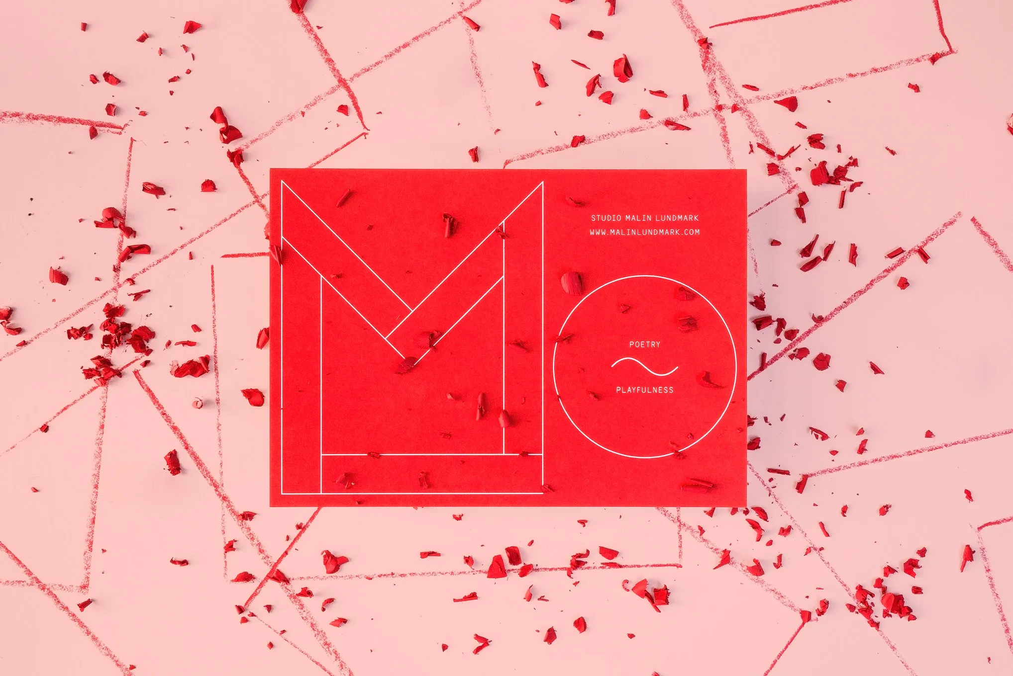 Red card with an outlined M and a circle reading “Poetry ~ Playfulness”, among red crayon shavings