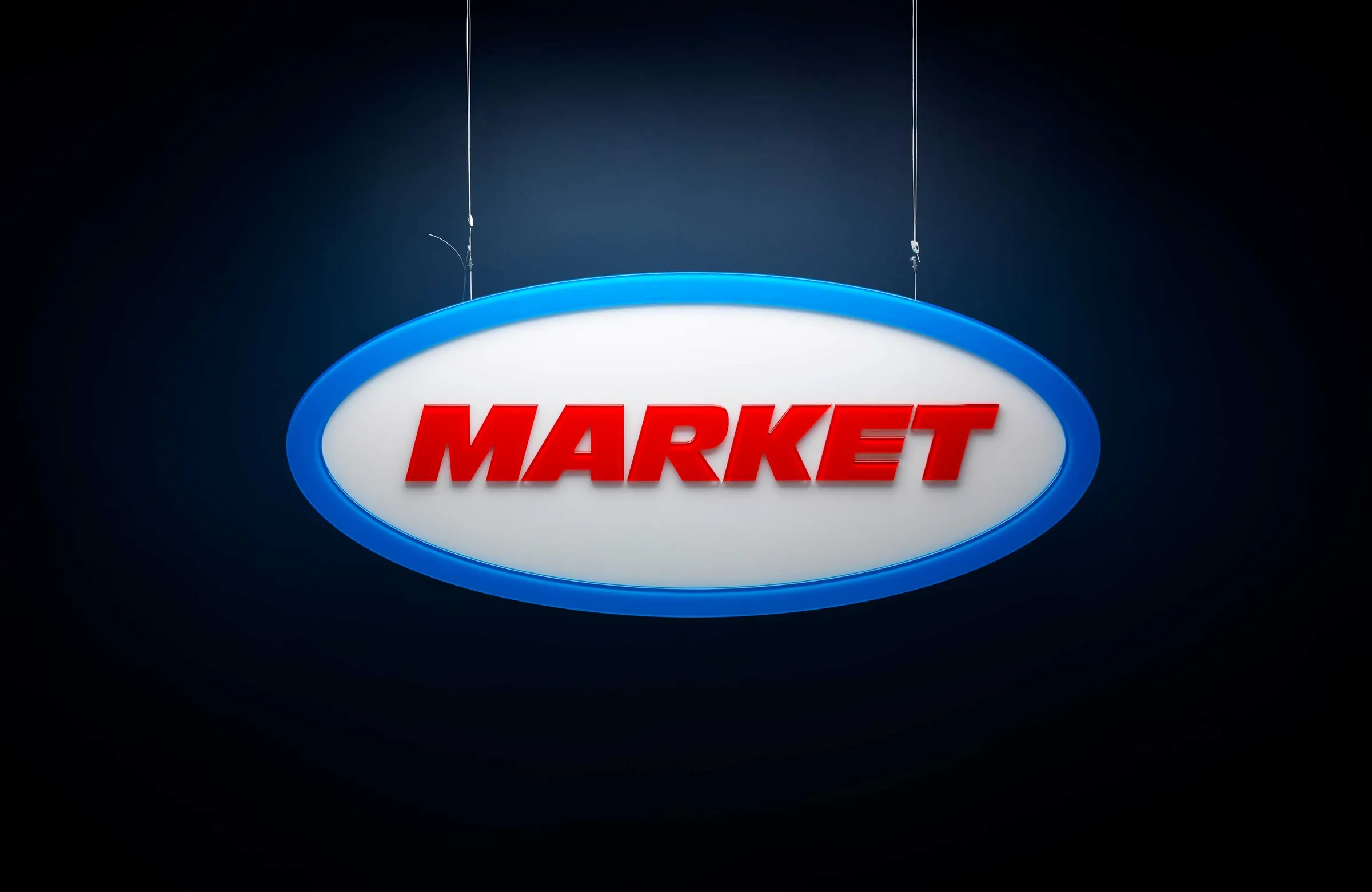 Oval Market sign hanging on wires against a dark blue backdrop