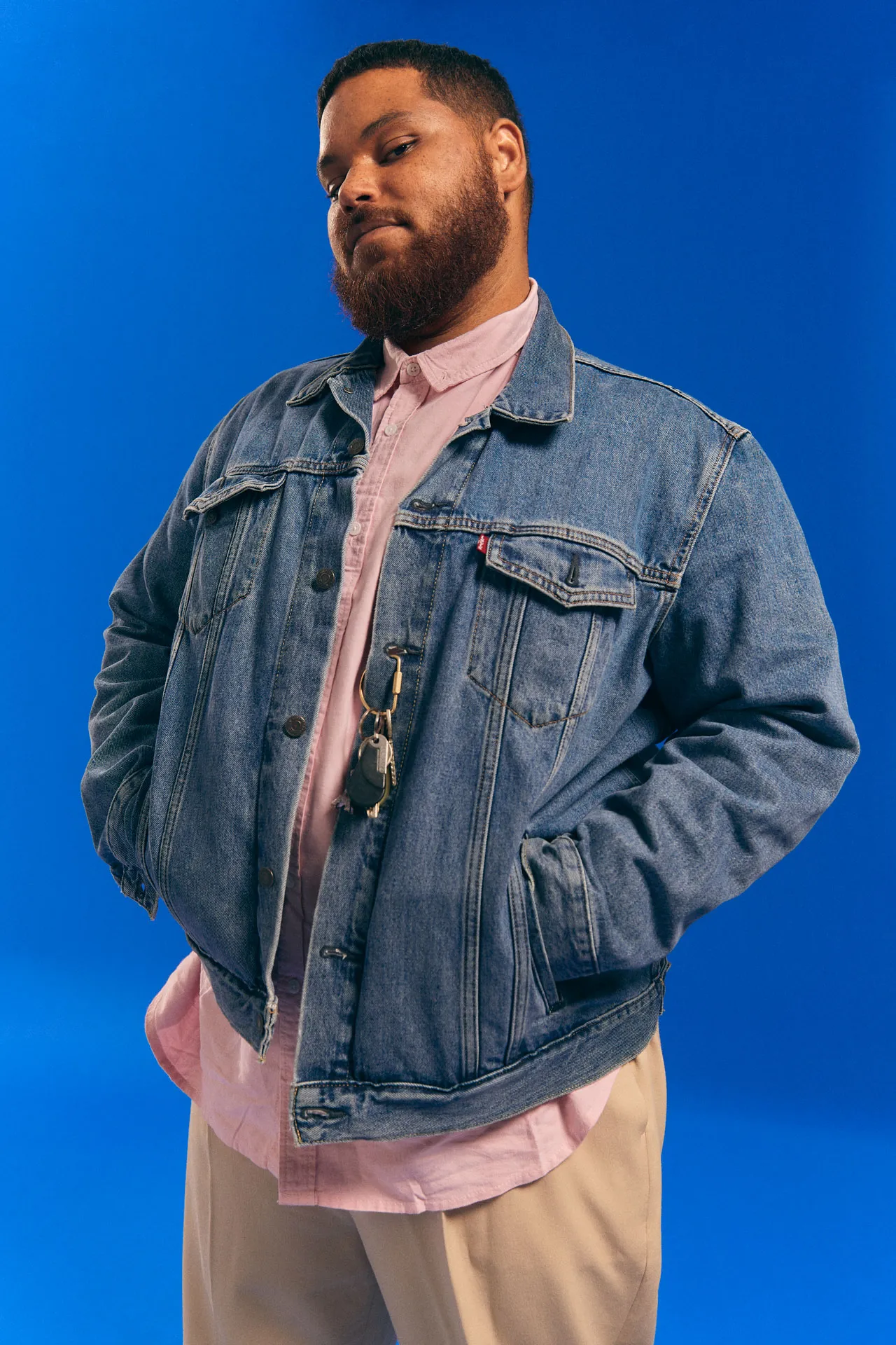 Campaign portrait: a bearded man in a denim jacket and pink shirt against blue