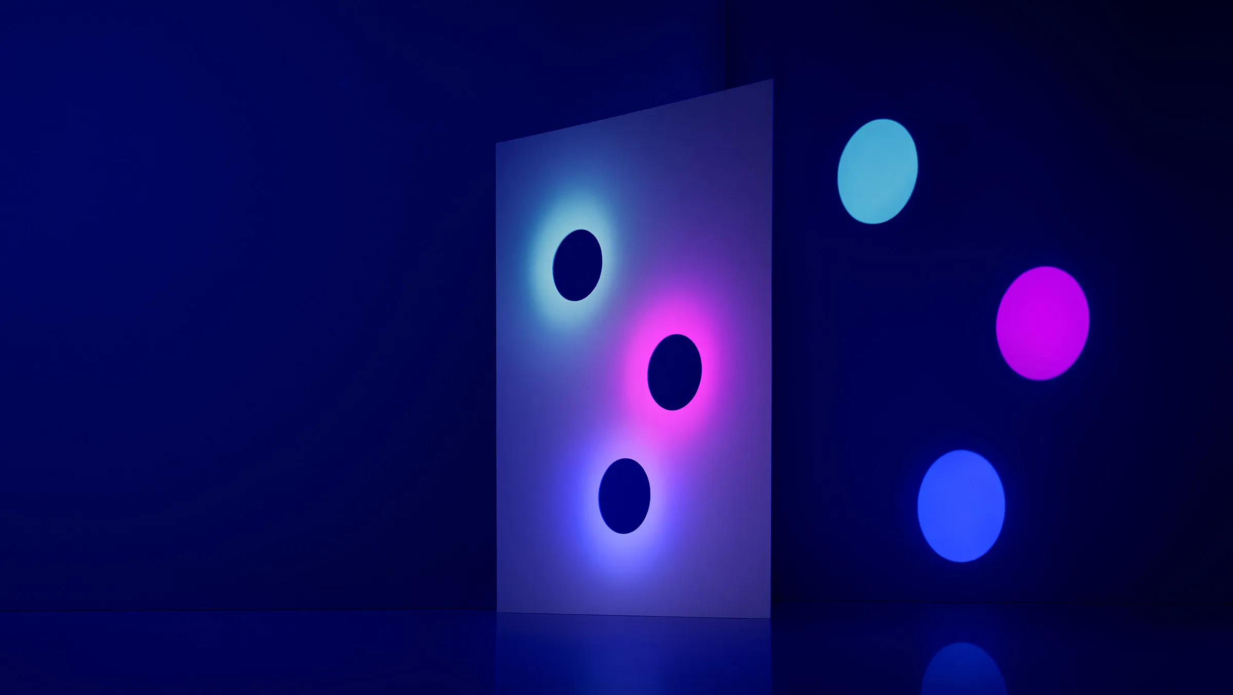 Panel with three holes glowing cyan, pink and blue, throwing coloured discs onto a dark blue wall