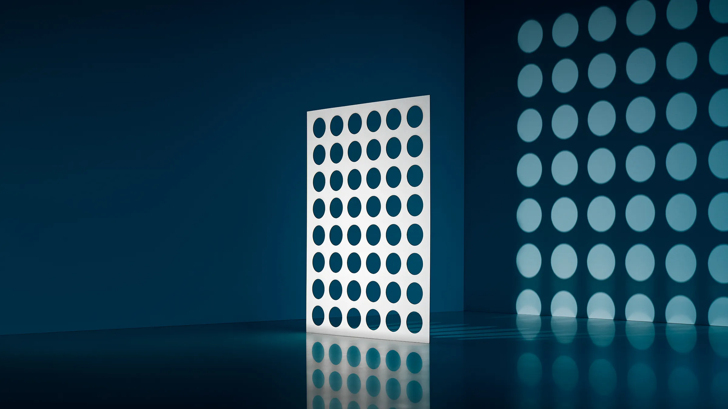 White panel with large round holes, casting rows of light circles onto a teal wall