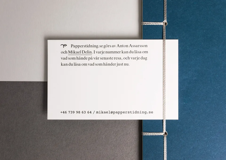 White card with serif text and a contact line, tucked under the string binding of a blue booklet