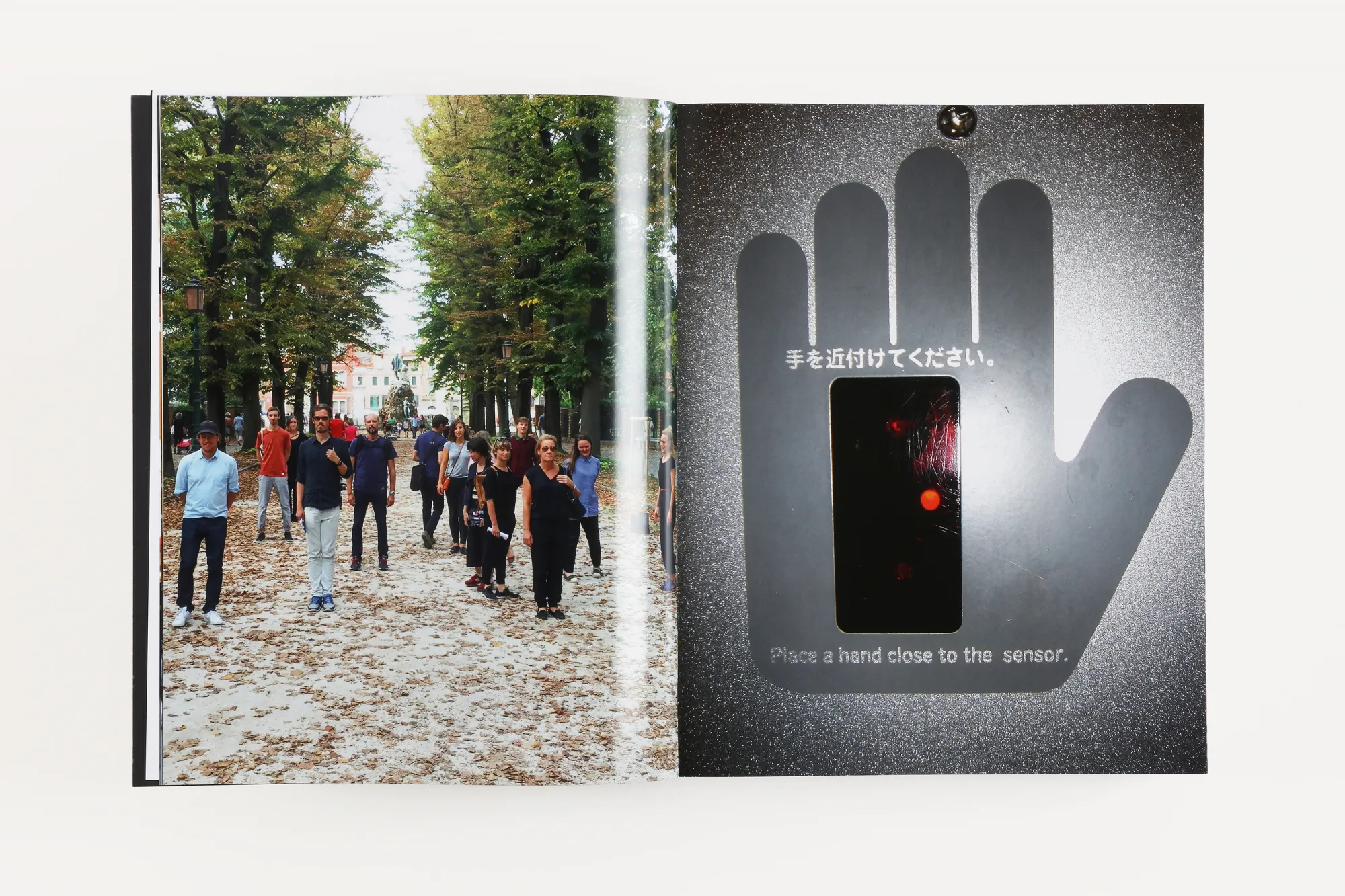 Open book spread: a group of people in an autumn avenue, and a hand-shaped sensor panel