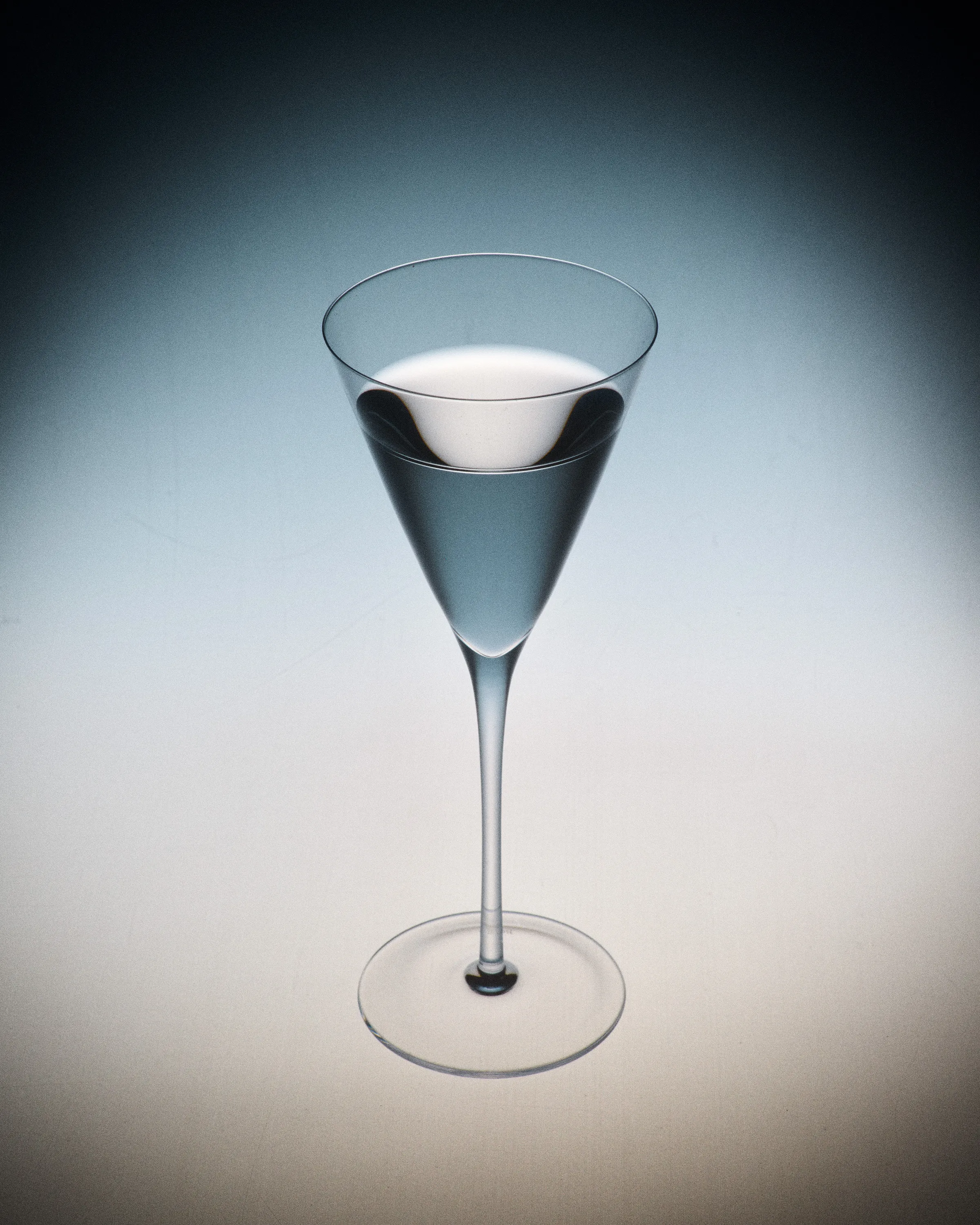 A clear cocktail in a tall, narrow V-shaped glass against a blue-to-cream gradient