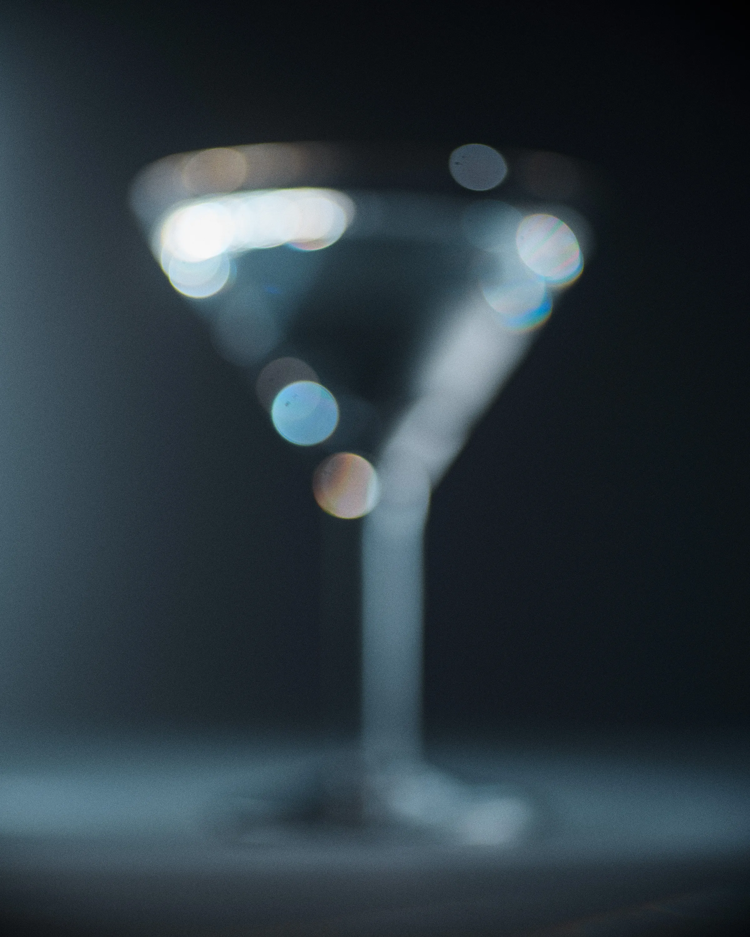 A blurred cocktail glass in dark blue light, scattered with soft circles of light