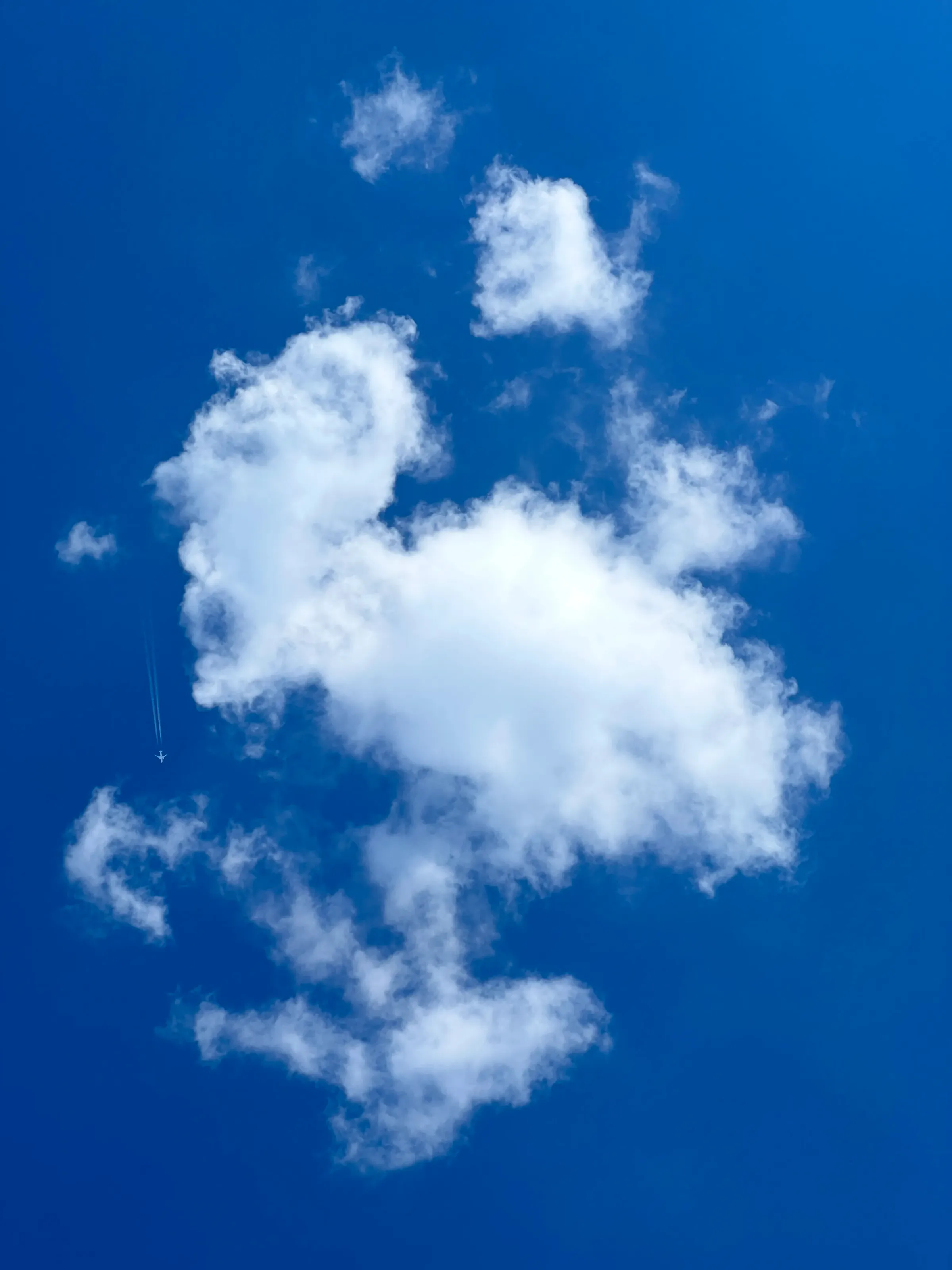 White clouds on a deep blue sky, a plane’s contrail at the left edge